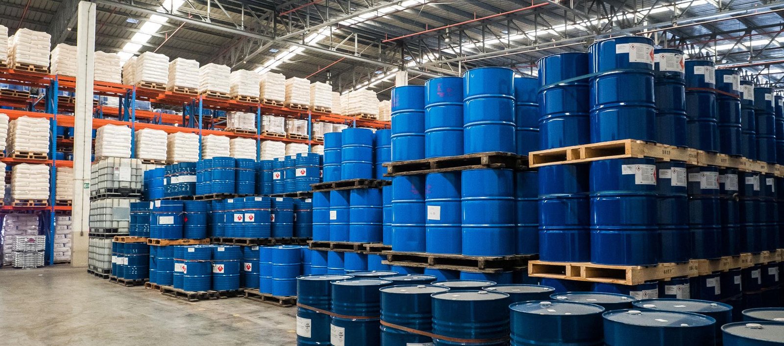 Blue chemical drums and packaged raw materials stored in an industrial warehouse